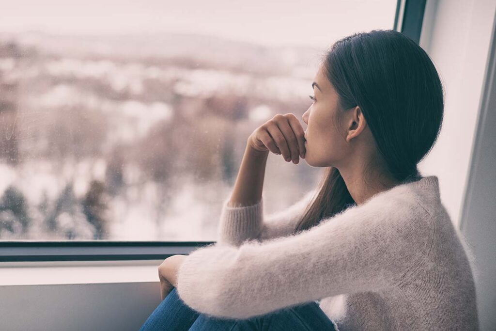 woman looking out window dealing with seasonal depression