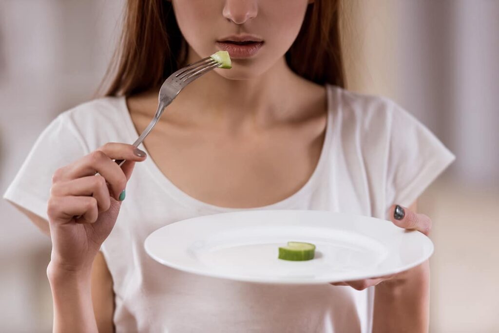 a woman stares at half a slice of cucumber and wonders about common types of eating disorders