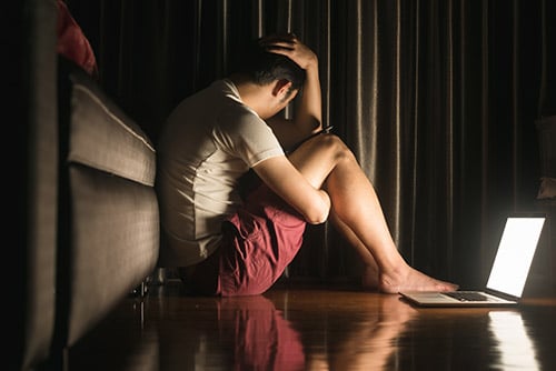 person sitting in the dark with laptop experiencing depressive disorders