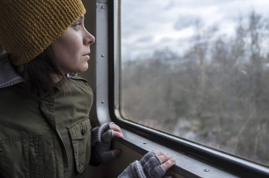 A woman stares out a window and wonders "Do I need mental health treatment?"