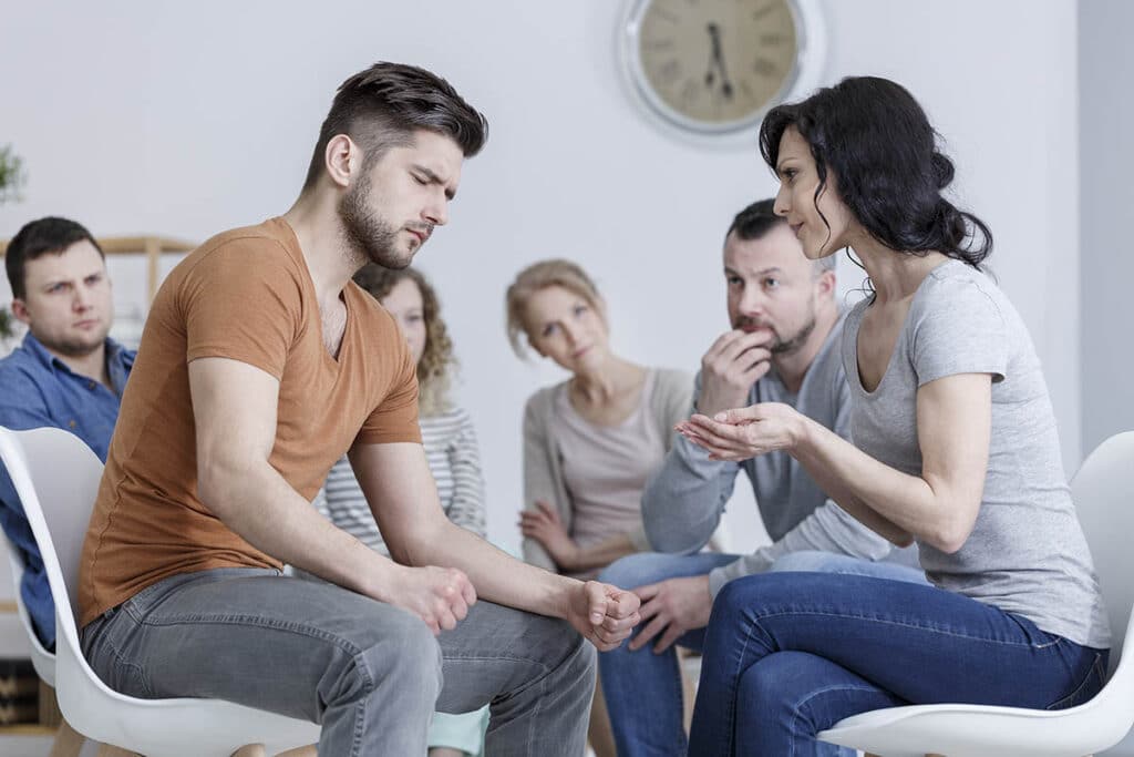 a group of people sit in a circle as a man wonders does my loved one need anger management