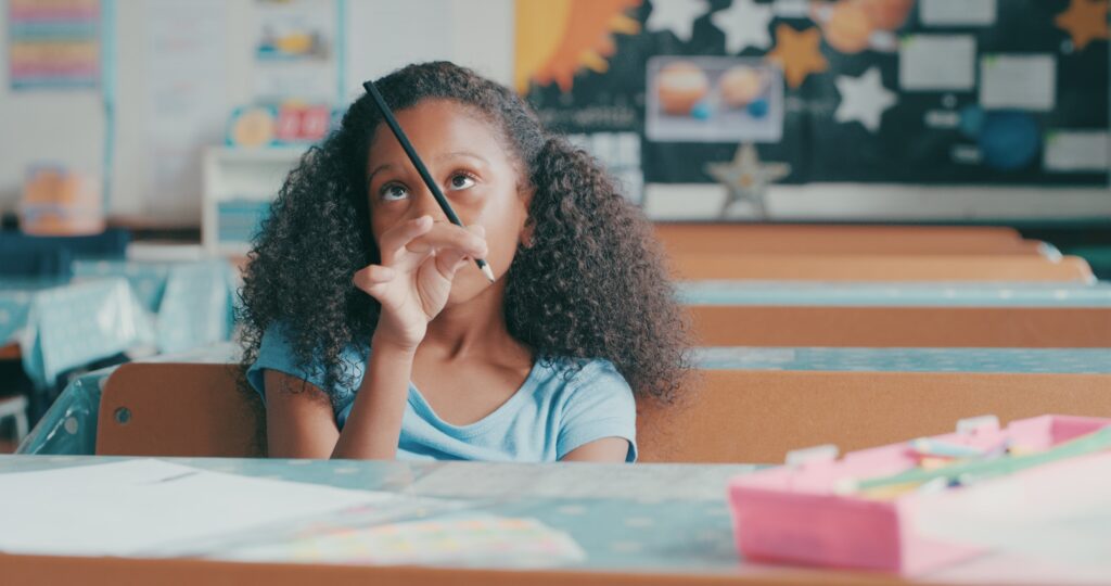 young girl looking bored while playing at a school desk