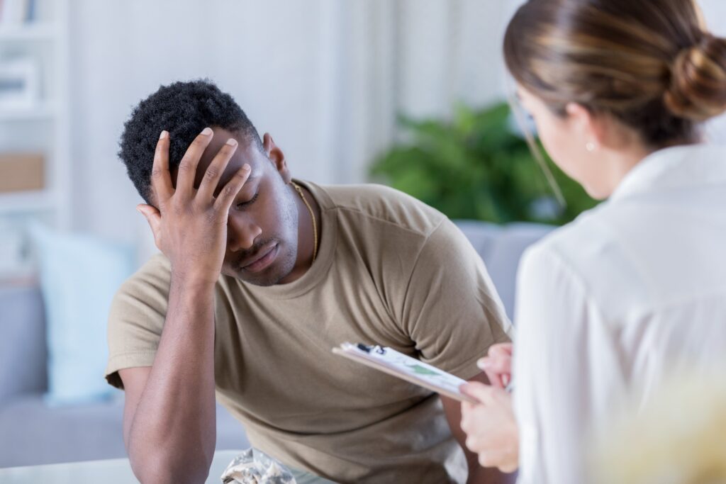 Distraught African American soldier has is head in his hands while talking with a healthcare professional