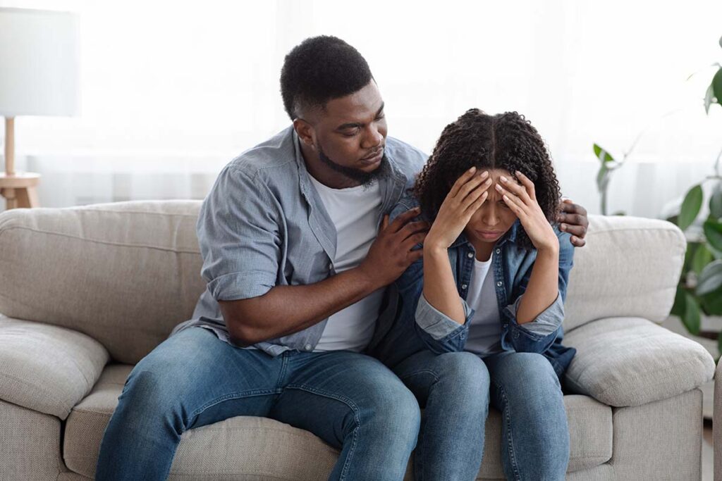 couple on couch with supportive partner comforting other partner