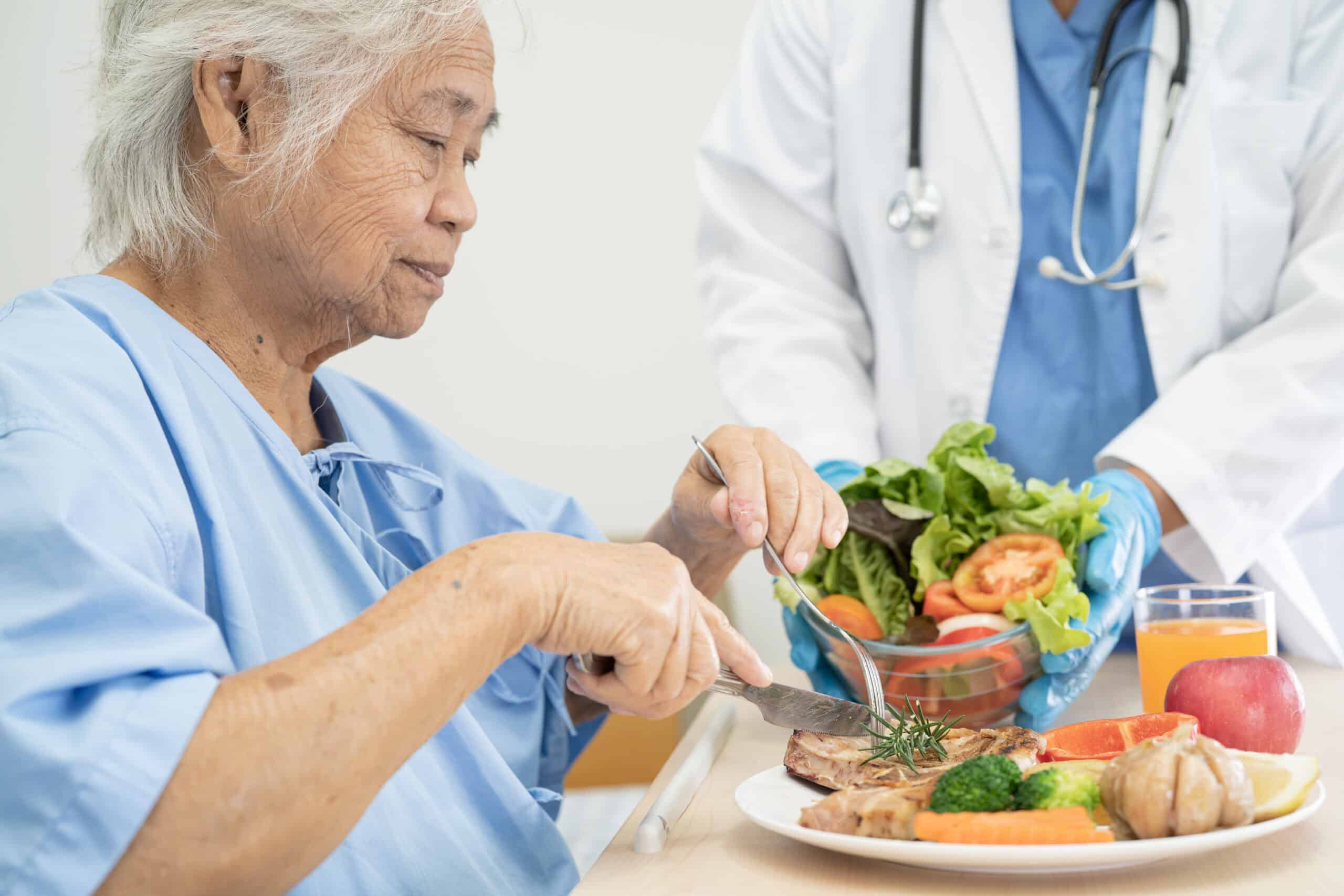 Asian senior or elderly old lady woman patient eating breakfast and vegetable healthy food with hope and happy while sitting and hungry on bed in hospital.