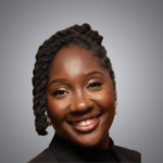 A woman with dark skin and braided hair smiles at the camera. She is wearing a black top and earrings, with a gray gradient background behind her.